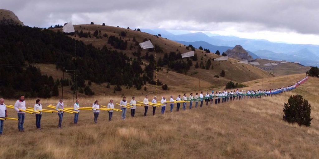 200 personnes en ligne tiennent chacune deux flûtes éoliennes sur la corniche de la montagne de Céüse