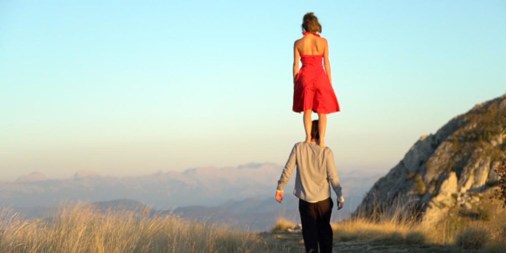 Justine, un femme en robe rouge est debout sur les épaules d'un homme, Frédéri