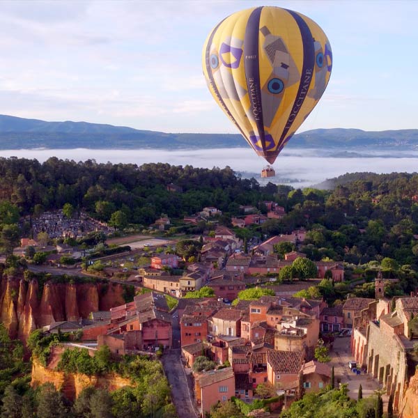 une montgolfière de L'Occitane en Provence survole un village du Lubéron