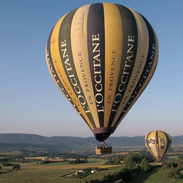 deux montgolfières jaunes et bleues aux couleurs de l'Occitane en Provence volent au dessus des champs