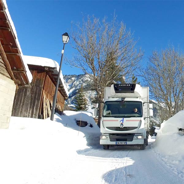 un camion blanc Alpagel effectue une livraison dans un village de montagne enneigé